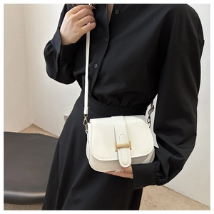Close-up of a white saddle crossbody bag with a gold H-shaped clasp on a black dress
