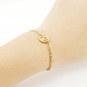 Close-up of a delicate 18K gold stainless steel chain bracelet with a round M-letter charm