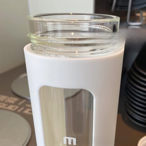 Detail of round cup mouth and white protective sleeve on minimalist glass water bottle