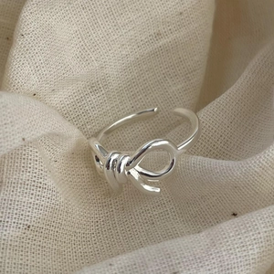 Detailed shot of a minimalist silver ribbon knot open ring on textured beige fabric