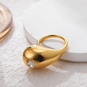 Detailed view of a gold teardrop ring with a faceted clear gemstone on white texture