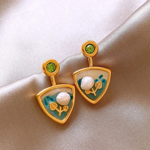 Macro shot of gold floral earrings with fresh pearls and green gemstones on silk