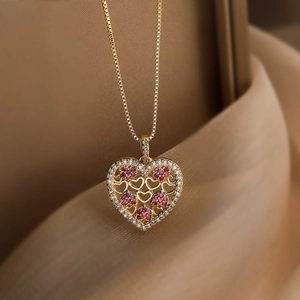Detail of 18K gold plated heart pendant with filigree patterns and pink stones