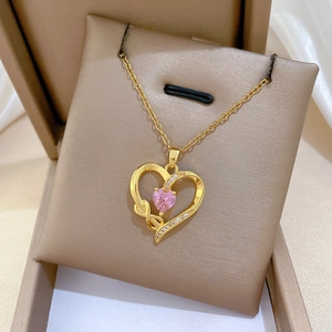 Macro detail of gold bow necklace with pink heart gemstone on brown velvet box