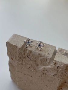 Macro detail of silver flower stud earrings with blue gems and hammered metal texture