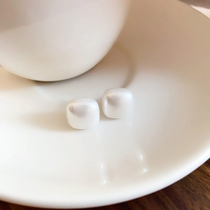 Detail view of square pearl stud earrings with gold plating on a white ceramic plate
