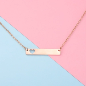 Macro detail of a rose gold bar necklace featuring a minimalist hollow heart pendant design