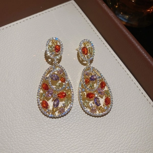 Detail of colorful oval gemstones set in gold openwork drop earrings on cream leather