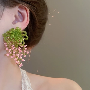 Detail of handmade green and pink floral beaded tassel earrings worn by a model
