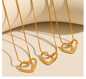 Trois colliers cœur dorés avec chaîne serpent fine sur un fond blanc minimaliste