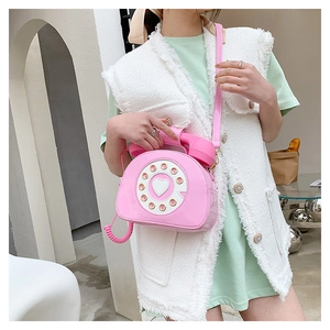 Close-up of a pink retro telephone crossbody bag worn by a model in a white vest