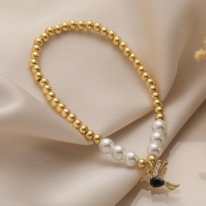 Elegant elastic pearl bracelet with gold beads and a bird pendant featuring black gemstone