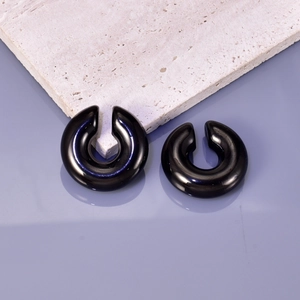 Close-up of high-polish black C-shaped hoop earrings on natural white stone base