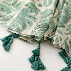 Detailed macro view of tropical green leaf pattern scarf with dark green tassel trim