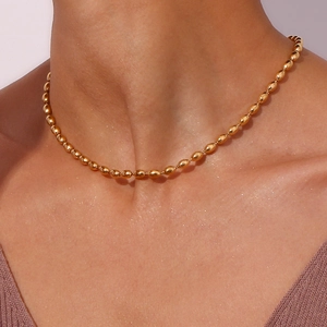 Detail of elegant gold beaded chain necklace worn on neck featuring oval metallic beads