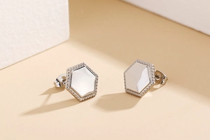 Macro detail of silver hexagonal stud earrings with beaded edges on a beige background