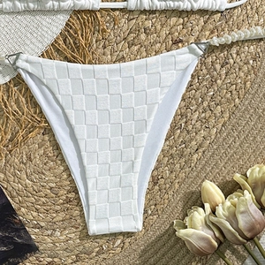 Detail view of white checkered bikini bottoms featuring elegant pearl side straps on a mat