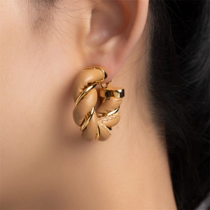 Close-up of twisted gold metal and beige woven leather hoop earrings on a model