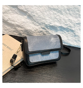 Detail of blue denim crossbody bag featuring black trim and gold-toned metal hardware