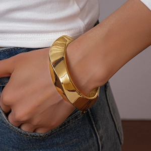 Close-up of a chunky twisted gold bangle on model wrist with minimalist denim outfit