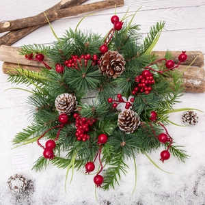 Christmas wreath with green pine needles, natural pine cones, and red berries on white wood