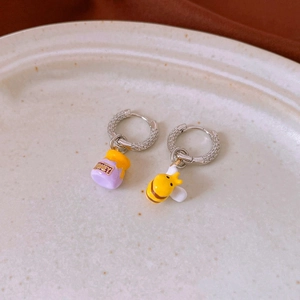 Detailed view of asymmetric bee and purple honey pot charms on silver hoop earrings