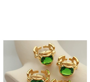 Detail of adjustable gold rings featuring emerald green crystals on a beige jewelry stand