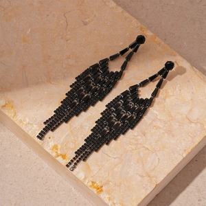 Détail de boucles d'oreilles pampilles en zircon noir sur pierre de marbre beige