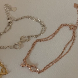Detail of three-tone twisted double-chain bracelets with X symbol and heart charm