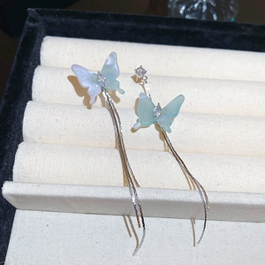 Macro shot of silver asymmetrical butterfly earrings with long tassels and blue resin wings