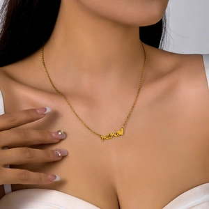 Close-up of a gold-tone Mama letter pendant necklace with a small heart on a model's neck