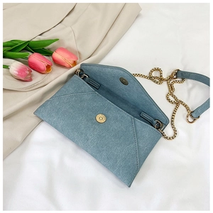 Detail of light blue denim envelope bag with gold magnetic buckle and chain strap
