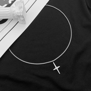 Detailed view of silver cross necklace with center clear gemstone on black backdrop