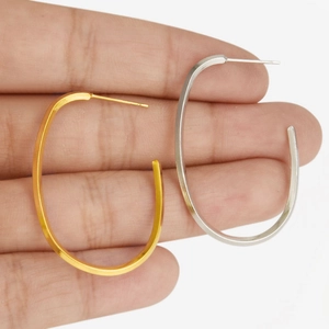 Detail shot of large oval hoop earrings in gold and silver held to show size scale