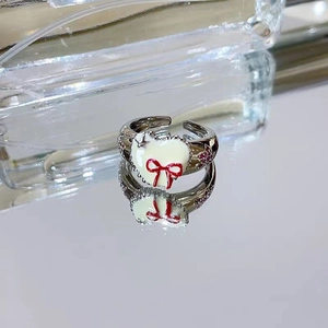 Detail of silver heart ring with white enamel and red bow on a reflective surface