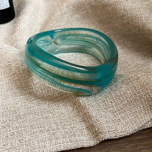Detailed macro shot of a turquoise resin open bangle with natural fluid texture on fabric