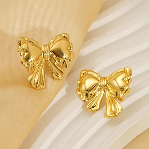 Polished gold bow earrings with textured ribbon details on a minimalist display stand