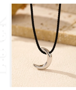 Macro shot of silver crescent moon pendant with black cord on stone texture