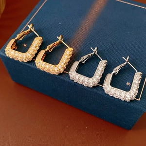 Détails de créoles carrées en zircon or et argent sur un coffret à bijoux bleu foncé