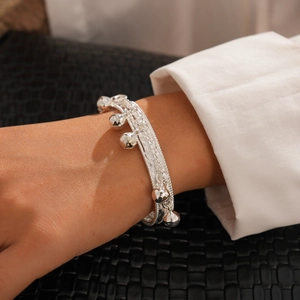 Détail d'un bracelet argenté avec clochettes porté par un mannequin sur fond de cuir