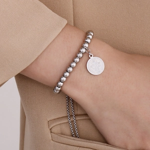 Dettaglio del bracciale con perline argentate, medaglia San Benedetto e nappine al polso