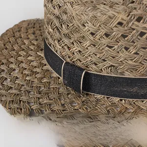 Detail of natural seagrass weave texture and black decorative ribbon on a flat top straw hat