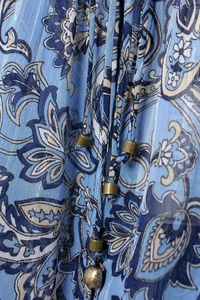 Dettaglio in chiffon blu con motivo paisley, laccetti e perline metalliche in ottone
