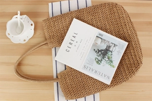 Flat lay of a woven straw shoulder bag with a Cereal magazine on a light wooden table