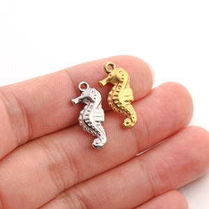Macro view of gold and silver seahorse charms on a fingertip for DIY jewelry making