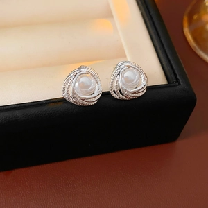 Macro shot of silver pearl stud earrings with woven swirl texture on black leather box