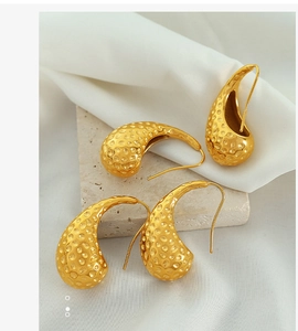 Detailed close-up of 18K gold teardrop earrings with textured hammered finish on silk