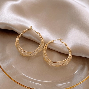 Detail of twisted gold hoop earrings with zircon crystals on silk fabric