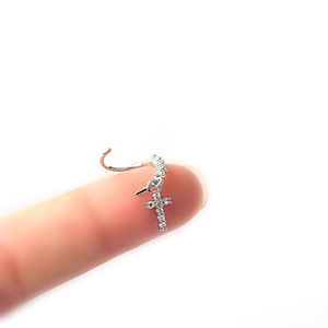 Silver nose ring with sparkling zircon cross pendant shown on fingertip detail