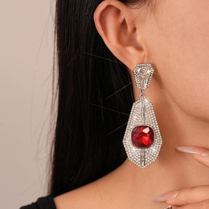 Macro detail of geometric silver earrings featuring a large red gemstone and zircon pavé